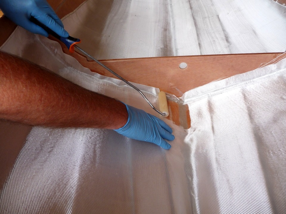La résine époxy est déposée au rouleau sur le tissu. Elle "mouille" le tissu en éliminant l'air entre ses fibres et le colle à la surface du contreplaqué. 